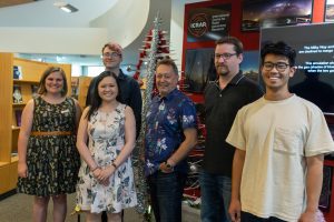 The six members of the AusSRC team standing next to a SKA Christmas tree antenna decorated in tinsel, baubles and a Christmas star on top. December 2021