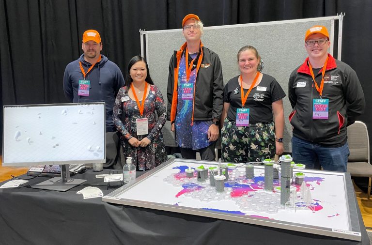 five people standing behind a table with a marble race activity and a computer screen on it