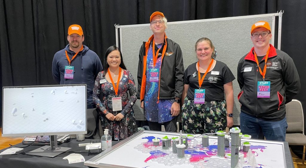 five people standing behind a table with a marble race activity and a computer screen on it