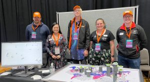 five people standing behind a table with a marble race activity and a computer screen on it