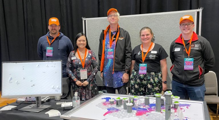 five people standing behind a table with a marble race activity and a computer screen on it